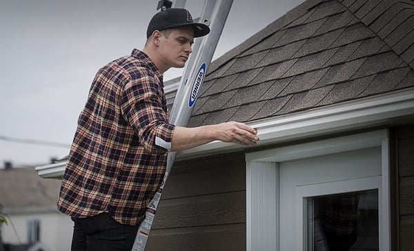 Person on a ladder inspecting their gutters